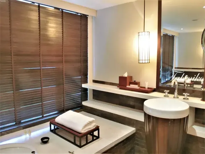 Modern bathroom with wooden blinds, a white sink, and a towel on a bench.