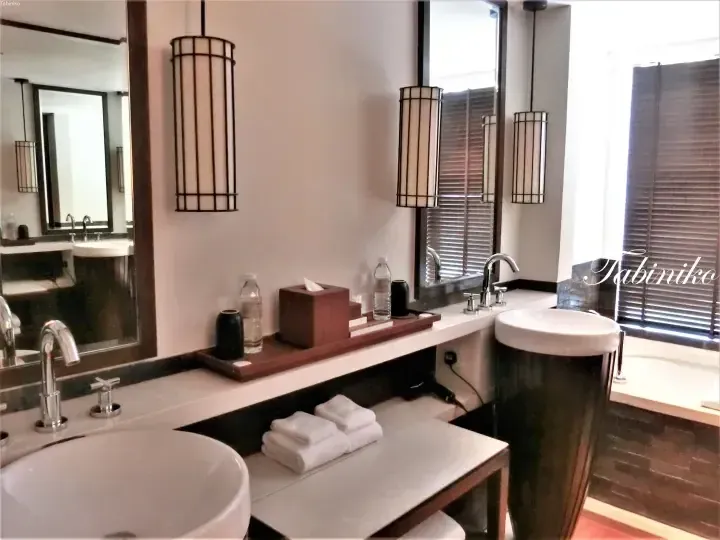 Modern hotel bathroom with dual sinks, wooden accents, and hanging lantern-style lights.