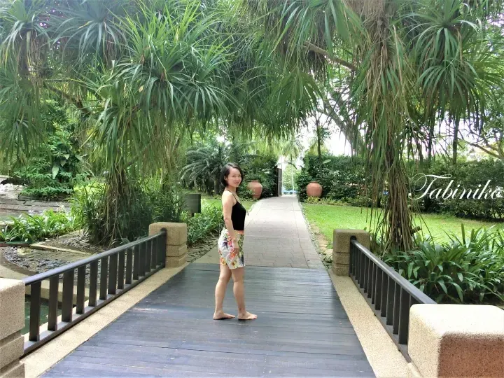 Woman standing barefoot on a wooden bridge in a lush tropical garden at a resort.