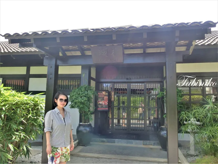 瓦屋根と木造の外観が特徴的な日本家屋風の建物の入り口前に立つ女性。看板には「湖月 KOGETSU」と記されている。