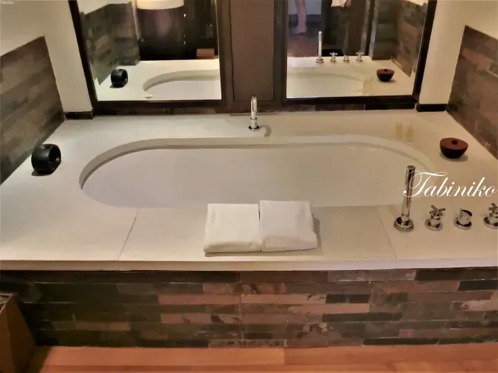 Luxury spa bathtub with white towels and dark stone accents in a modern bathroom setting.