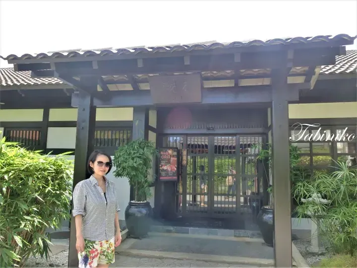 A woman stands in front of the entrance to Kogetsu, a traditional Japanese-style building with a tiled roof and wooden structure.
