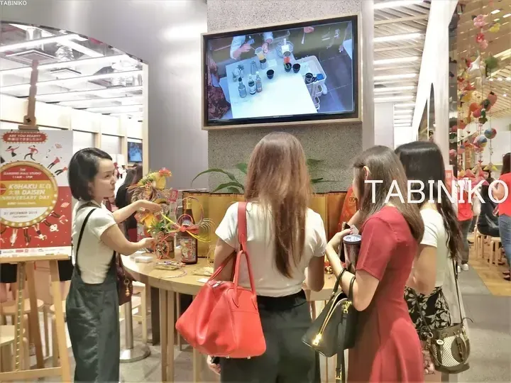 Women at a TABINIKO event in a Malaysian mall, watching a screen and interacting with a display.