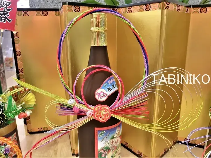Decorated sake bottle with colorful ribbons and a gold screen backdrop for a festive occasion.