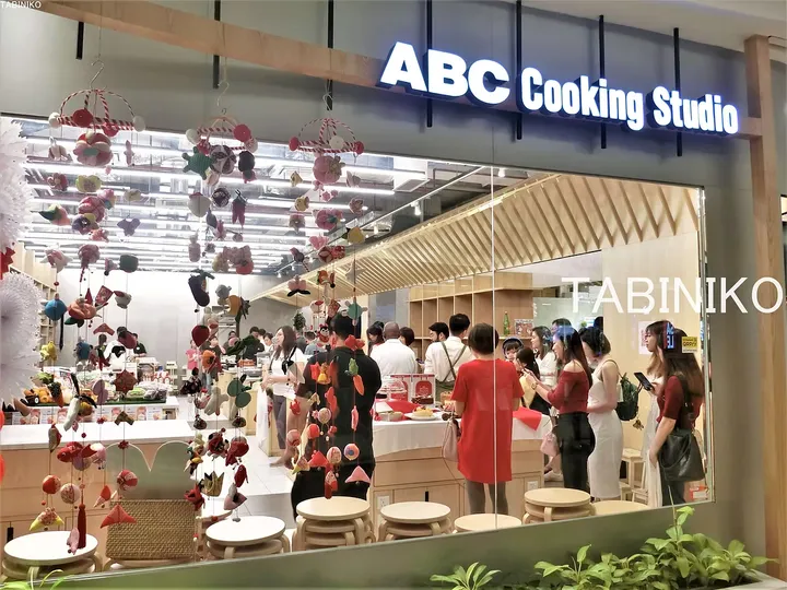 カラフルな吊り飾りと店内の客が見えるABC Cooking Studioの外観。