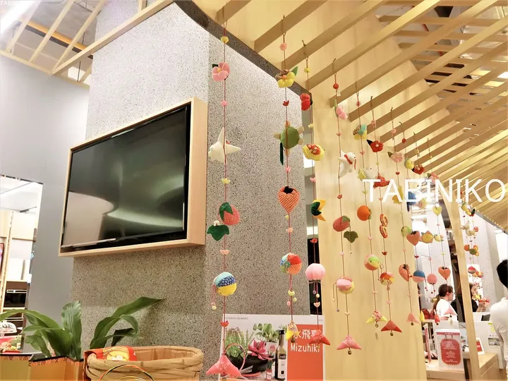 灰色の壁にテレビが掛けられたモダンな空間に、木製の天井からカラフルな布風鈴が飾られている。