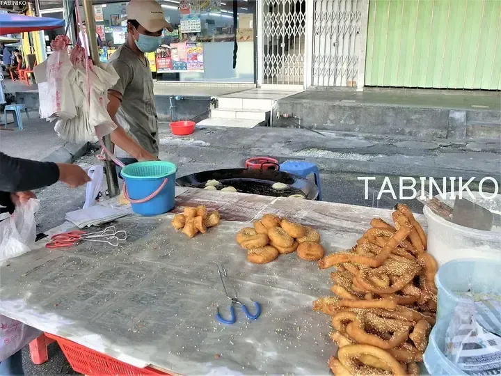 A street vendor prepares and sells traditional fried dough snacks, including sesame-covered twists, at an outdoor stall.