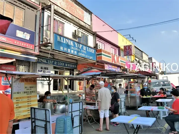 Street scene at KK Super Mart and Klinik Yap & Looi with food stalls and customers dining outdoors.