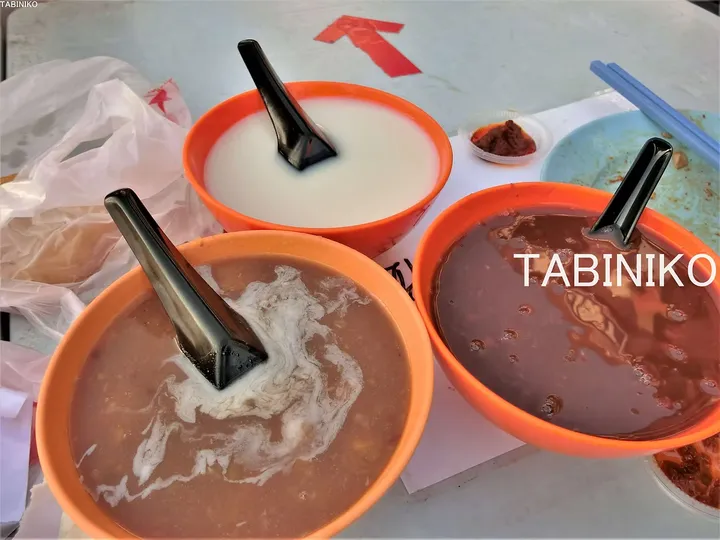 黒いスプーンが添えられた、白いミルク、赤豆スープ、チョコレートデザートが入った3つのオレンジ色のボウル。