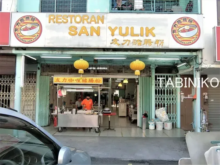 Restoran San Yulik storefront with yellow lanterns and staff preparing food at the counter.