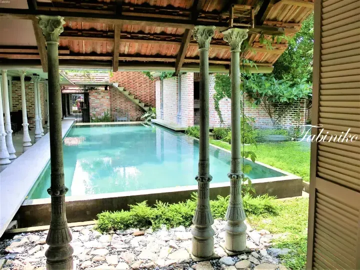 A serene swimming pool surrounded by ornate columns and red brick walls at a heritage property.