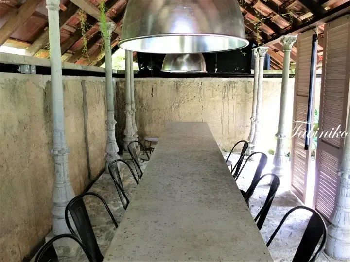 Long concrete dining table with black chairs under vintage metal pendant lights in a rustic heritage building.
