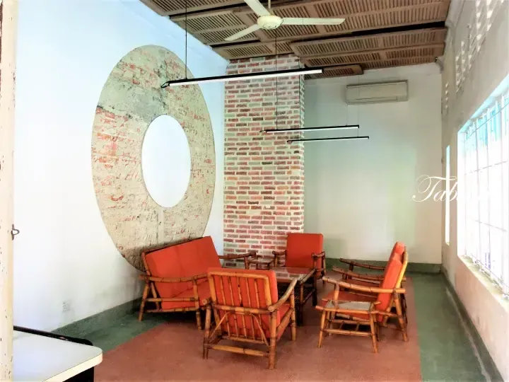 Cozy lounge area with rattan furniture and orange cushions, featuring exposed brick walls and a large circular architectural detail.