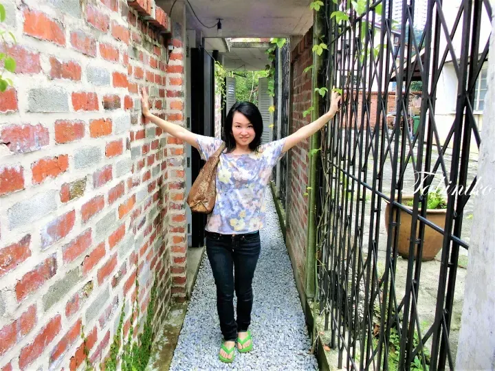 Woman posing in a narrow brick alleyway with a black metal gate, showcasing a charming heritage property in Malaysia.