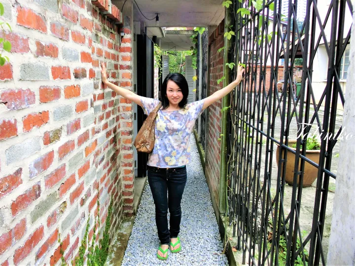 黒い金属製のゲートとレンガ壁の狭い路地でポーズを取る女性。マレーシアの魅力的な歴史的建物の雰囲気を伝えています。