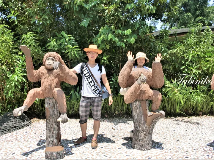 マレーシアの緑豊かな公園で、オランウータンの像と記念撮影をするカップル。
