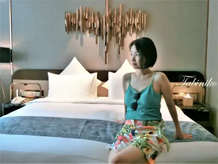 Woman sitting on a hotel bed with a modern copper wall art installation above the headboard.