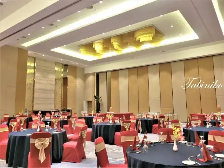 Elegant banquet hall with round tables, red chairs, and gold chandeliers at a luxury venue