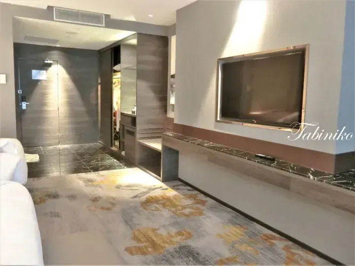 Modern hotel room interior with large TV, marble console, and patterned carpet.