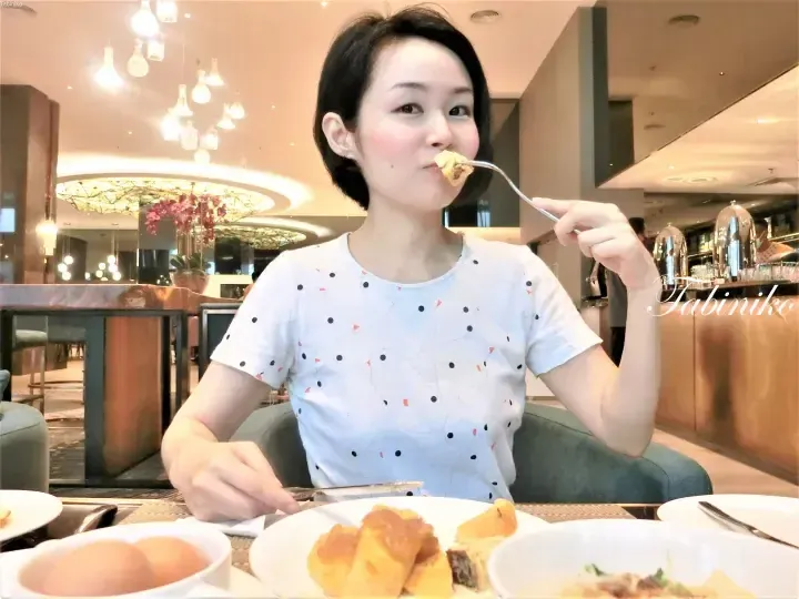 Woman eating breakfast buffet at a hotel restaurant with chandeliers and food on the table.