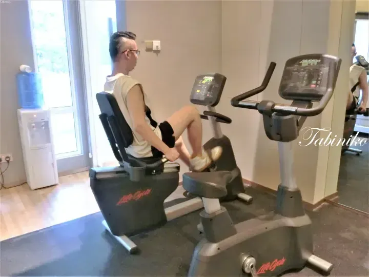 A man exercising on a recumbent bike in a hotel gym with a water dispenser nearby