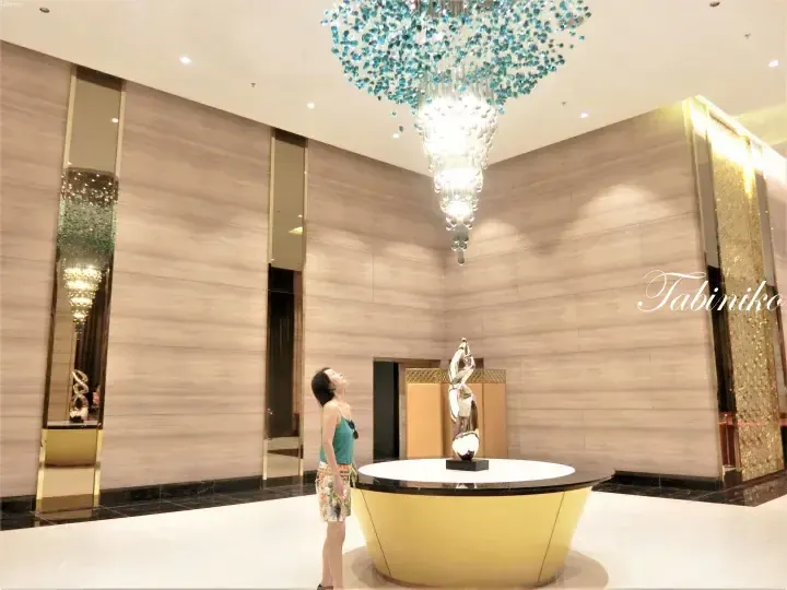 Woman admiring a large blue chandelier in a modern hotel lobby with marble walls and a silver sculpture.