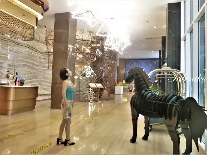 Woman admiring geometric ceiling lights in a modern hotel lobby featuring a large black horse sculpture.