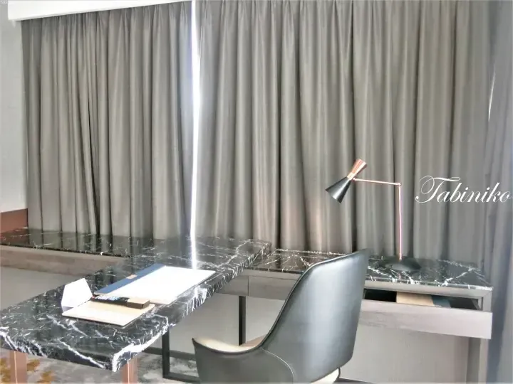 Modern hotel desk with black marble top, copper lamp, and grey curtains