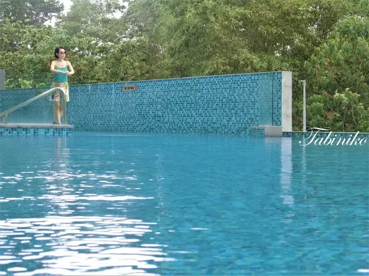 Woman standing by a blue tiled swimming pool with a no diving sign, surrounded by lush greenery.