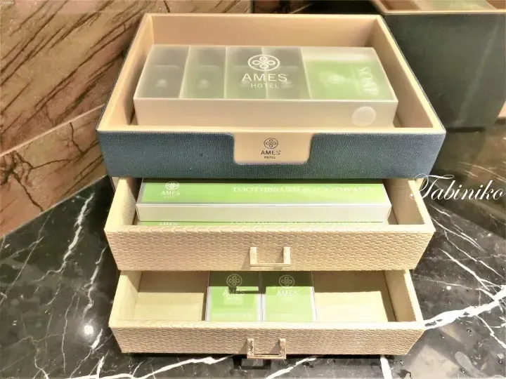 Amenities drawer set at AMES Hotel featuring toiletries, toothbrush, and sanitary bag in elegant packaging.