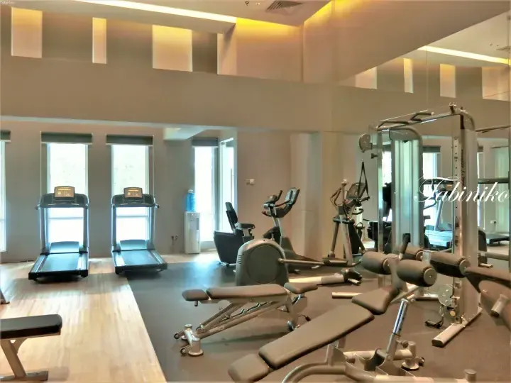 Modern gym with treadmills, elliptical machines, and weight benches in a bright room with large windows.