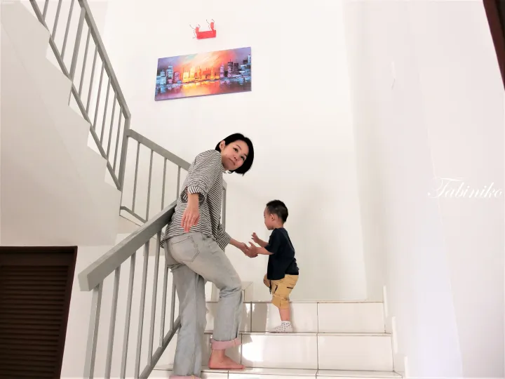 モダンな家の白いタイルの階段で、ストライプシャツを着た女性が幼児の手を握っている。