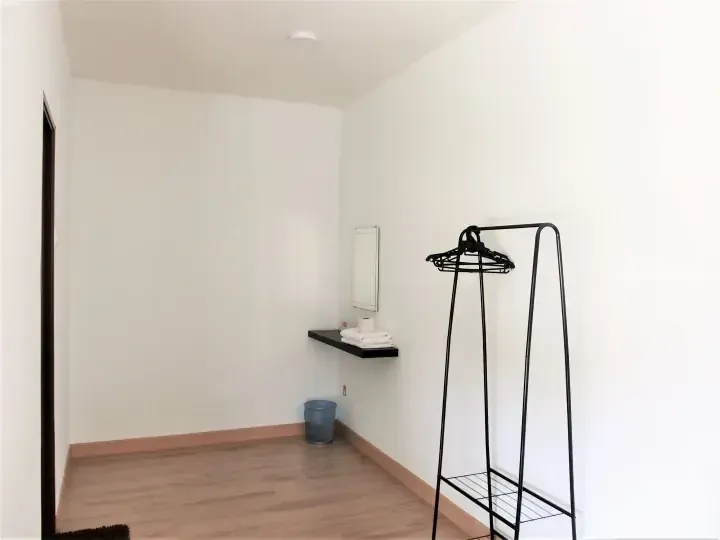 Minimalist room interior with white walls, wooden flooring, a black coat rack, and a floating shelf with folded towels.