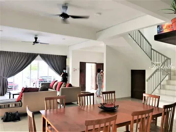 Spacious open-plan living and dining area with wooden table, sofa, and staircase in a modern Malaysian home.