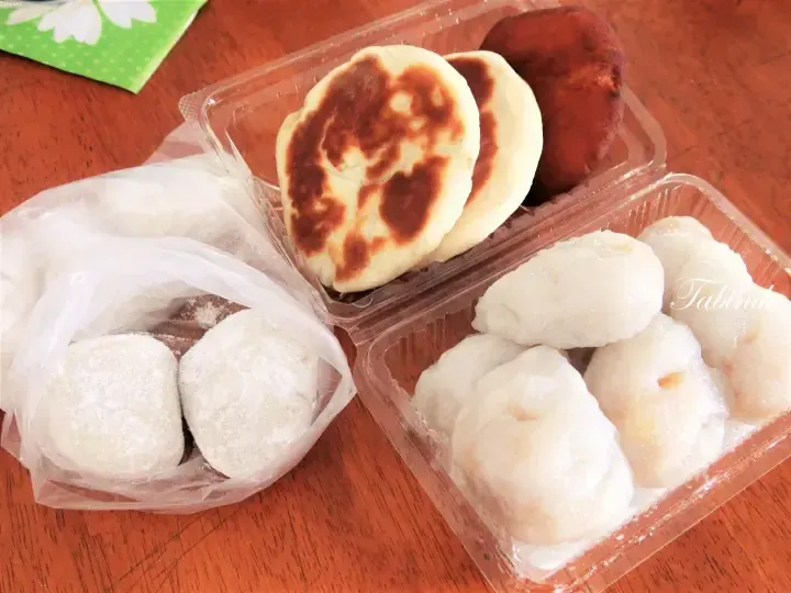 Assorted Malaysian snacks including grilled flatbread, glutinous rice balls, and steamed buns displayed in plastic containers.