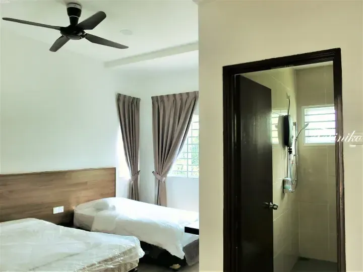 A bedroom with twin beds and a ceiling fan, featuring an open door revealing a tiled bathroom with a shower.