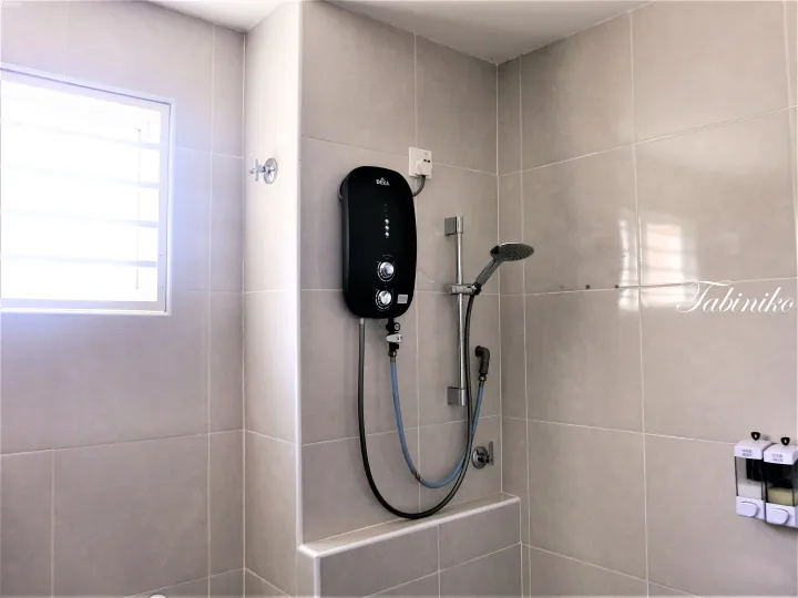 タイル壁に取り付けられた黒いDEKA式瞬間湯沸かし器とシャワーヘッド、石鹸ディスペンサー