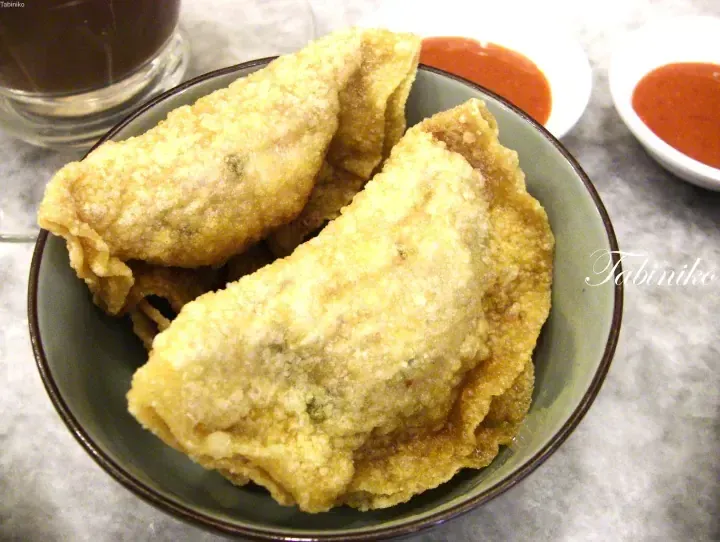 Golden crispy fried spring rolls served on a green plate with chili sauce and a glass of dark beverage.