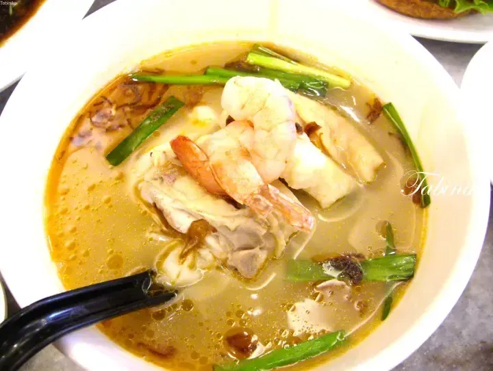 A bowl of creamy laksa soup with prawns, chicken, and green onions.