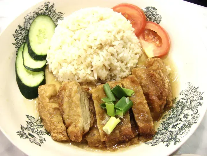 Sliced fried pork belly with rice, cucumber, and tomato on a decorative plate.