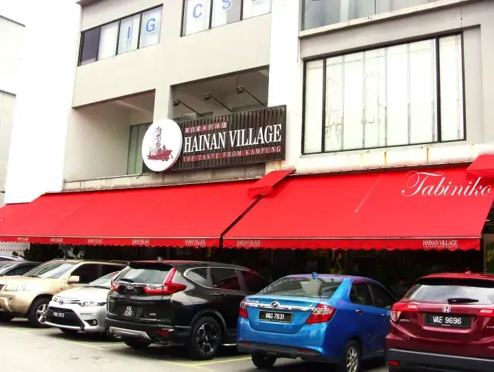 Hainan Village restaurant exterior with red awnings and parked cars
