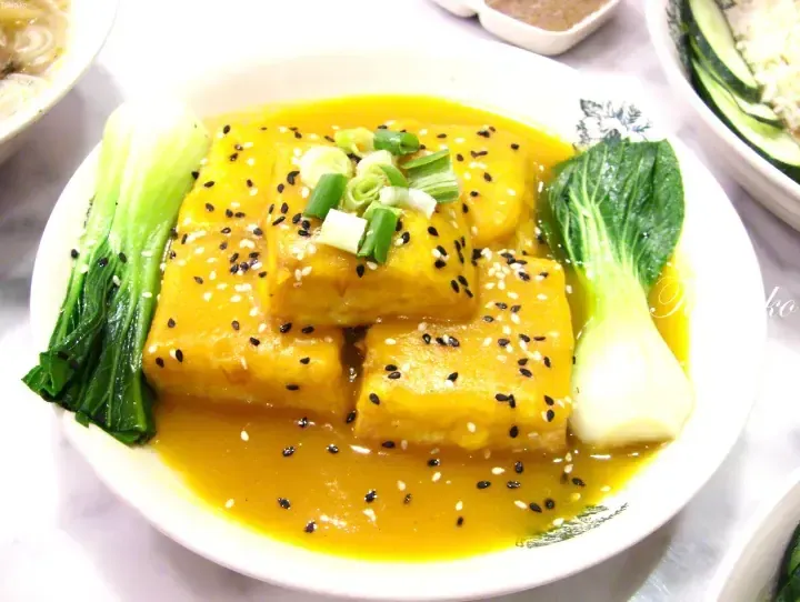 Golden curry tofu with bok choy and sesame seeds on a white plate