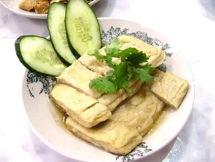 Sliced fried tofu with cucumber slices and cilantro garnish on a patterned plate