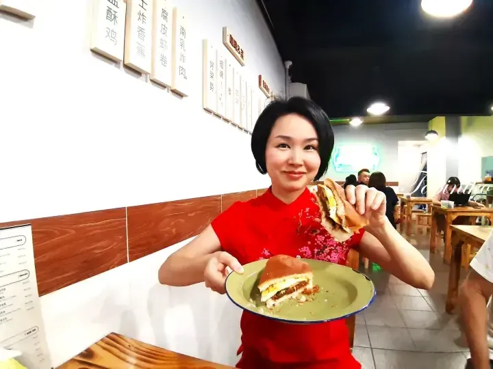 Woman in red cheongsam holding a sandwich in a Malaysian cafe with menu boards on the wall.