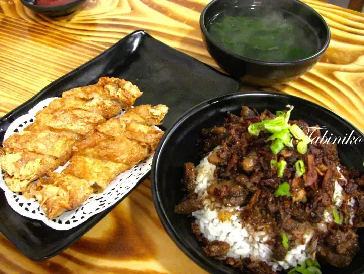 Crispy fried chicken served on a black rectangular plate alongside a bowl of rice topped with savory minced pork and a bowl of soup.