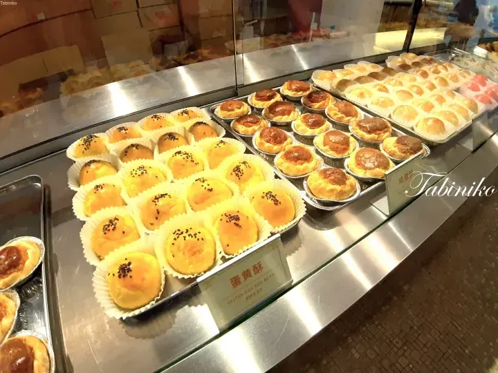 Display case featuring trays of golden salted egg red bean pastries and other baked goods at a Malaysian bakery.