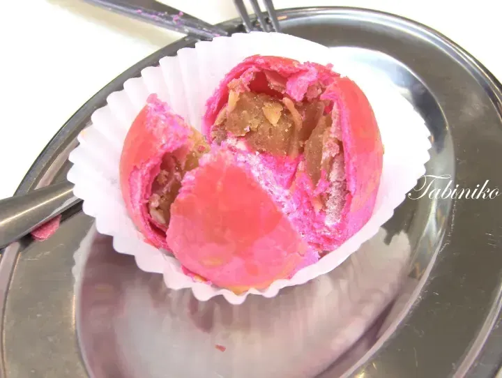 A vibrant pink pastry with a flaky crust and sweet filling sits in a white paper cup on a metal plate.