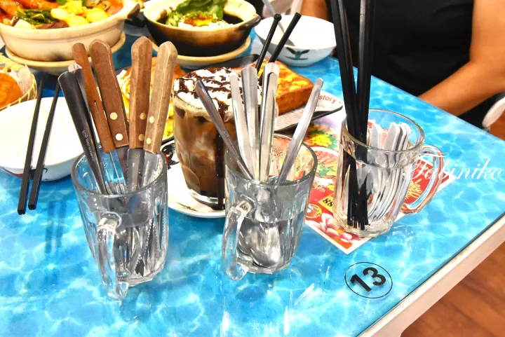 マレーシアの飲食店での青いテーブルに置かれたカトラリーやストローが入ったグラス、アイスカフェラテと料理。