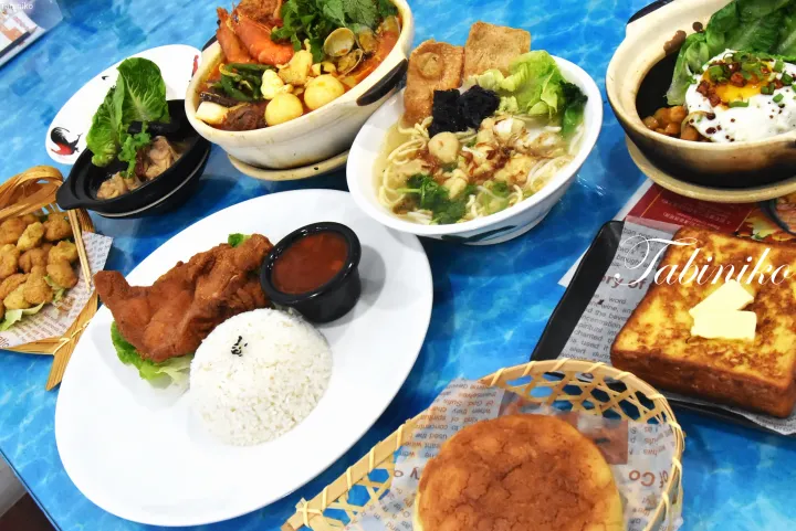 青いテーブルに並ぶマレーシア料理の盛り合わせ。ラクサ、土鍋飯、チキンライス、カーヤトーストなど。