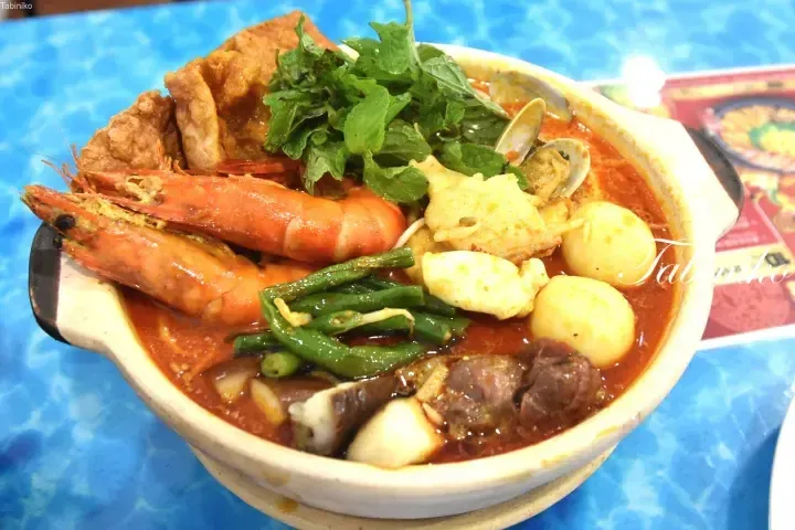 A claypot of spicy laksa with prawns, clams, tofu puffs, and herbs.